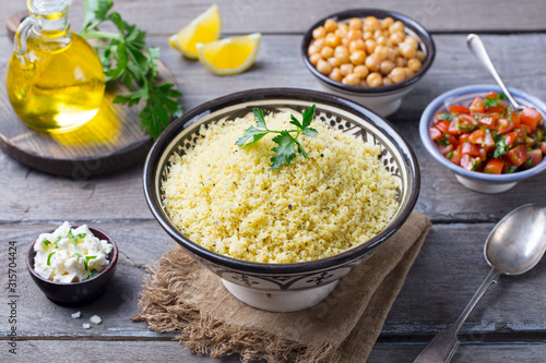 Couscous in bowl with olive oil. Wooden background. Close up.
