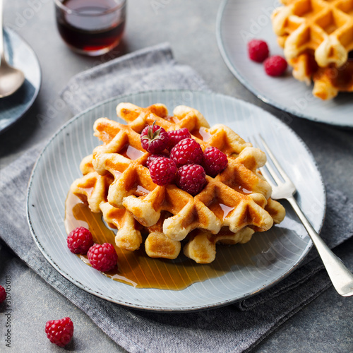 Breakfast Belgian waffles with maple syrup and fresh raspberry. Grey background.