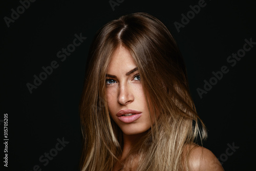 Beauty portrait of young blonde in a studio on a dark background