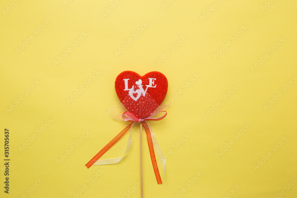 Fototapeta premium Closeup of a heart with a decor on a stick on a yellow isolated background. Spell love in white letters.