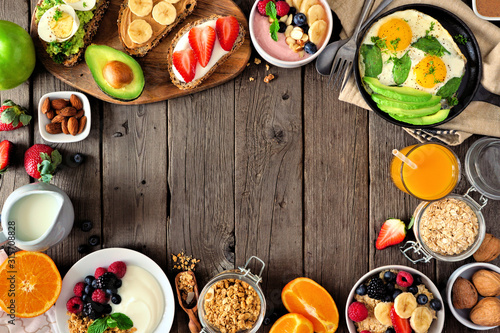 Healthy breakfast food frame. Table scene with fruit, yogurt, smoothie, oatmeal, nutritious toasts and egg skillet. Top view over a rustic wood background. Copy space.