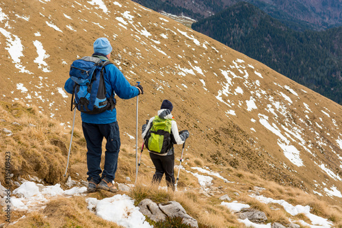 Картината върху платно Pair of hikers descending winter traile of grass covered slope.