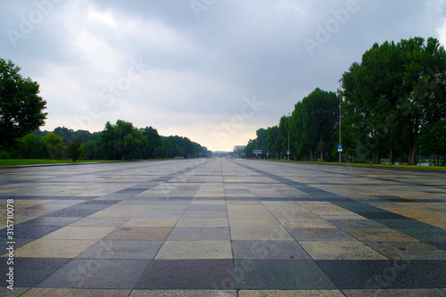 Fototapeta Naklejka Na Ścianę i Meble -  Empty Great Road in Nuremberg (Germany) - known landmark. The granite pavement is colorful and there are many green trees on the sides. It's a cloudy evening.  