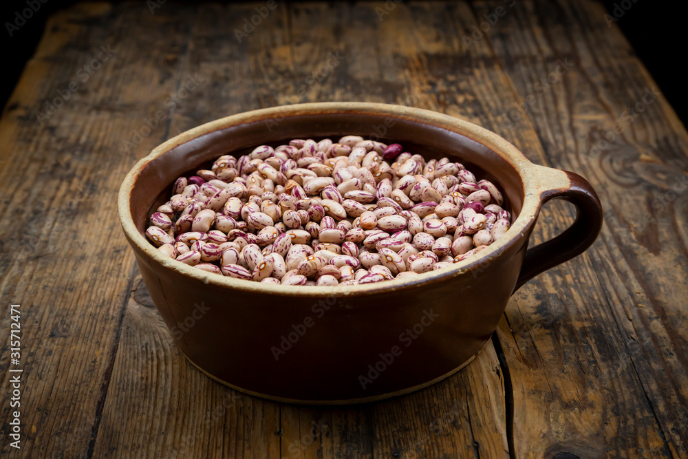 Bowl of dried pinto beans lying on wooden table Bowl of dried pinto beans lying on wooden table