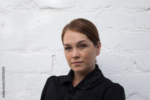 Portrait of serious caucasian middle aged woman looking at camera with soft look on the white brick background