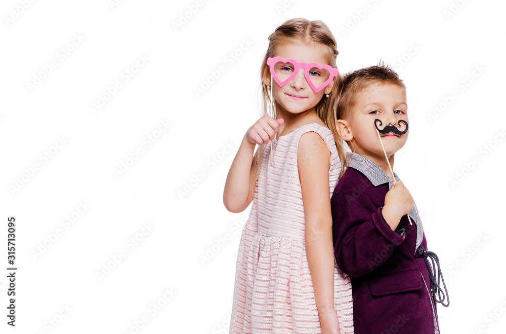 Girl with a heart-shaped cardboard glasses and a boy with a cardboard mustache posing on a white background Girl with a heart-shaped cardboard glasses and a boy with a cardboard mustache posing on a white background