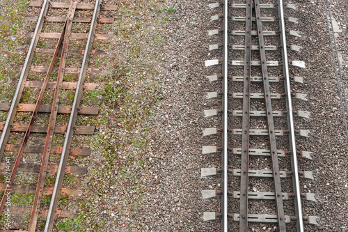 Two parallel railway tracks. top view. On left is old rusty road with wooden sleepers. On right is new shiny one with reinforced concrete support for rails