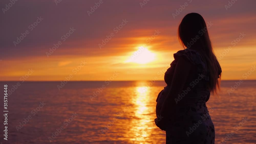 Silhouette of a young pregnant woman on a sunset background over the ocean Silhouette of a young pregnant woman on a sunset background over the ocean