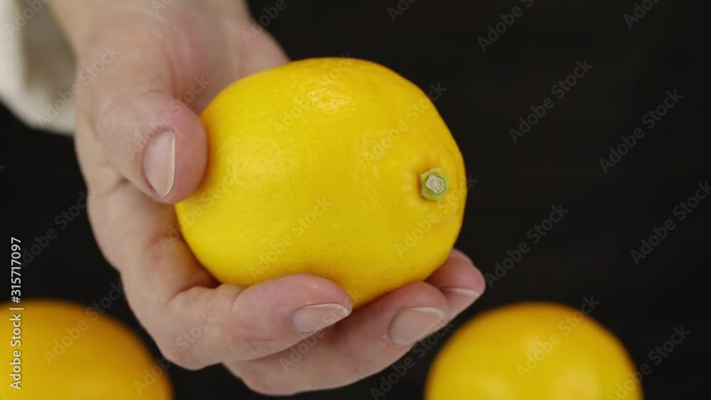 A female hand takes one of three lemons in the background and brings it to the foreground, close-up A female hand takes one of three lemons in the background and brings it to the foreground, close-up
