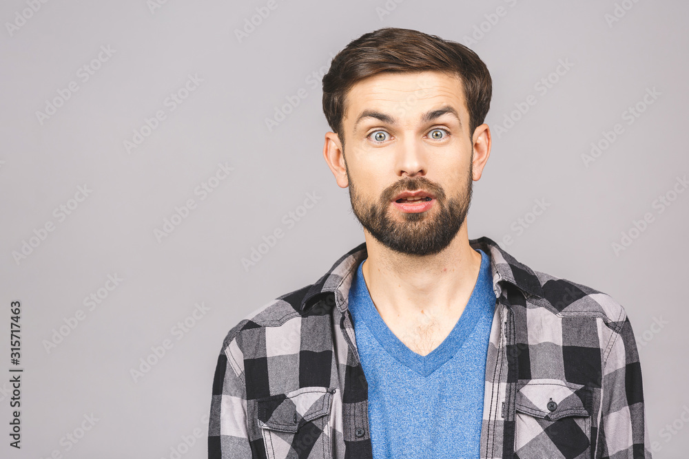 Obraz premium OMG! It's incredible! Portrait of handsome young man looking at camera while standing against isolated grey background. Close up portrait of bearded man keeping his mouth open.