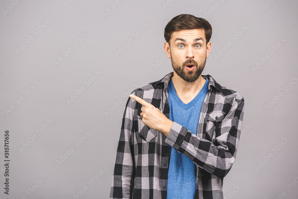 Young surprised man in blue t-shirt pointing right with his finger, shouting WOW, isolated on gray background with copy space fot your text. Shock content. Young surprised man in blue t-shirt pointing right with his finger, shouting WOW, isolated on gray background with copy space fot your text. Shock content.