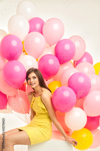 colorful portrait of young beautiful model with a lot of pink yellow and white baloons