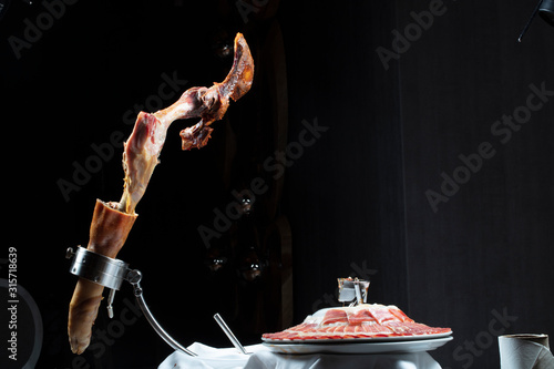 Jamón ibérico hueso y plato con jamón cortado sobre fondo negro. Iberian ham bone and plate with sliced ​​ham on a black background. 