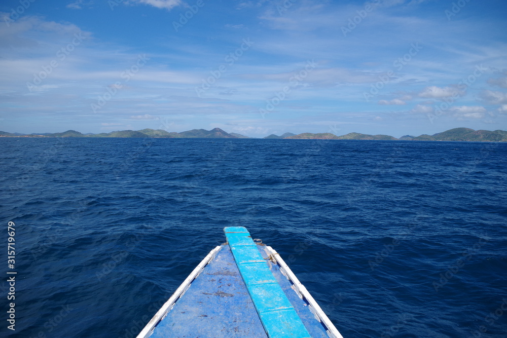 Obraz premium A view from a lone paraw boat sailing the Indian Ocean. On the horizon, many islands can be seen. The water is blue and calm. It's a warm sunny summer day and there are few clouds in the sky.
