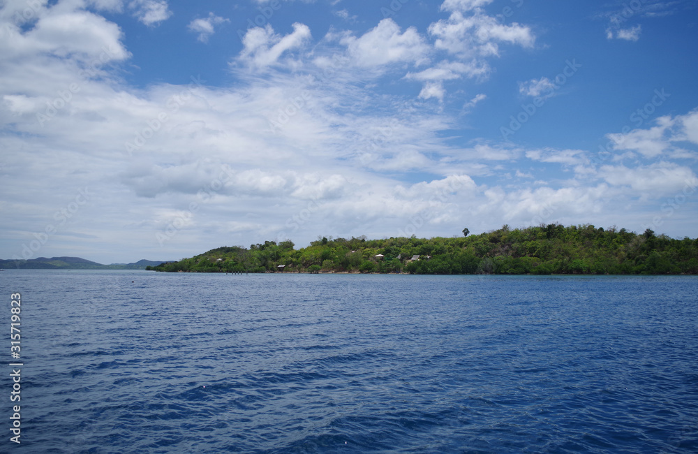 A small forested island in the Philippines archipelago. Isle is surrounded by the blue, calm waters of the ocean and azure, clear sky. There are few clouds, day is very bright and sunny. A small forested island in the Philippines archipelago. Isle is surrounded by the blue, calm waters of the ocean and azure, clear sky. There are few clouds, day is very bright and sunny.