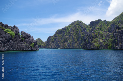 A big rocky island in the Philippines archipelago. The water of the ocean is calm and rippling slightly. The sky is clear and blue. It's a sunny warm summer day. 