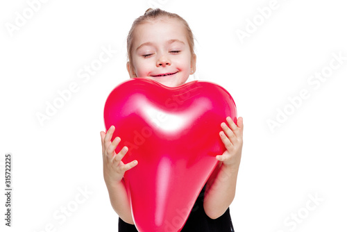 Little girl in a black elegant dress holding a red balloon in the shape of a heart on a white background