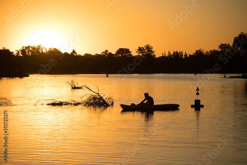 Kayaker silhouette at sunset on a river with floating logs and branches. Outdoor water sports