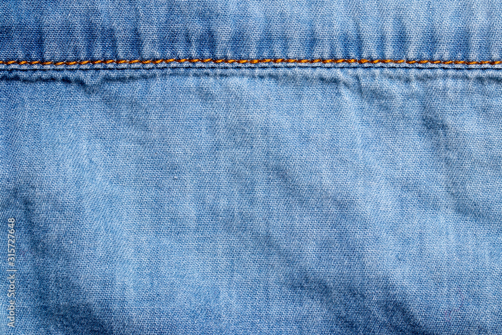 Denim background texture. Close-up of details of empty light blue jeans fabric jean surface with gold colored horizontal seam above. Macro. Top view. Beautiful backdrop with space. Denim background texture. Close-up of details of empty light blue jeans fabric jean surface with gold colored horizontal seam above. Macro. Top view. Beautiful backdrop with space.
