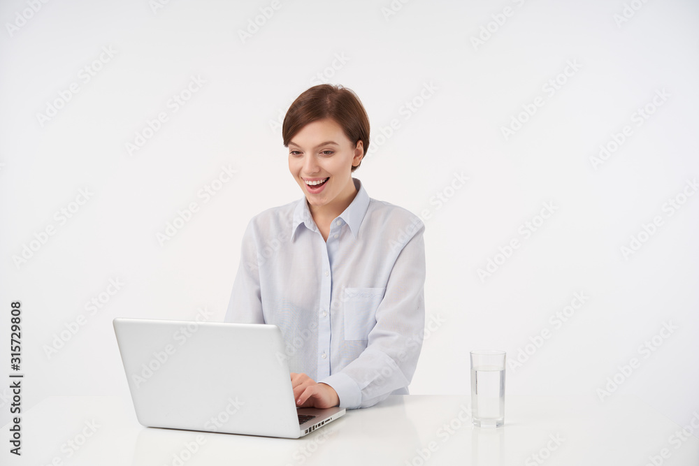 Joyful young brown haired pretty brunette lady with short trendy haircut wearing formal clothes while sitting over white background chatting with her colleagues and being in nice mood Joyful young brown haired pretty brunette lady with short trendy haircut wearing formal clothes while sitting over white background chatting with her colleagues and being in nice mood