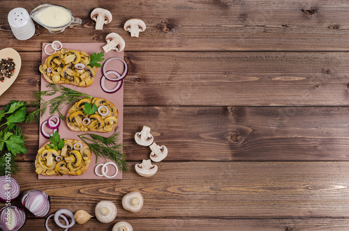 Sandwiches with fried champignons on a wooden board on a dark wooden background with ingredients and sauce with copy space. For advertising