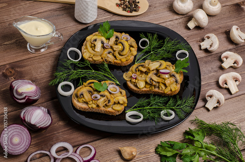 Sandwiches with fried champignons on a black plate on a dark wooden background with ingredients and sauce. For advertising