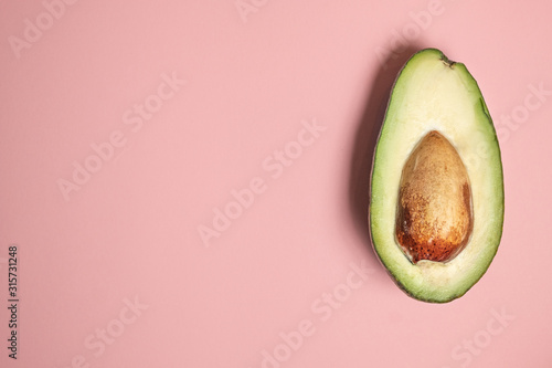 half avocado with a bone on a pink background. a beautiful combination of colors. vegan concept