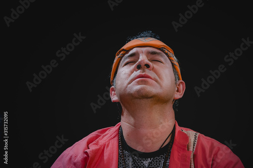 Shaman man, sorcerer, giving thanks duringPre-Hispanic ritual in Healing and cleaning with medicinal plants in Mexico, with black background photo