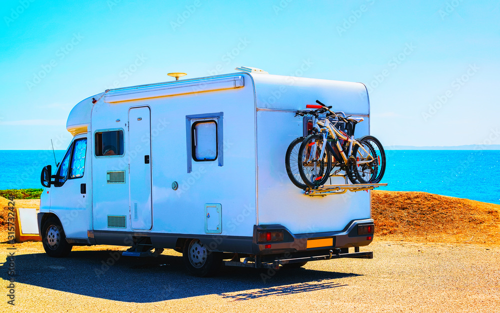 Camper with bicycle on road at Capo Pecora resort at Mediterranean sea in Sardinia Island, Italy summer. Caravan motorhome on holidays at highway. Minivan rv on motorway. Cagliari. Mixed media.