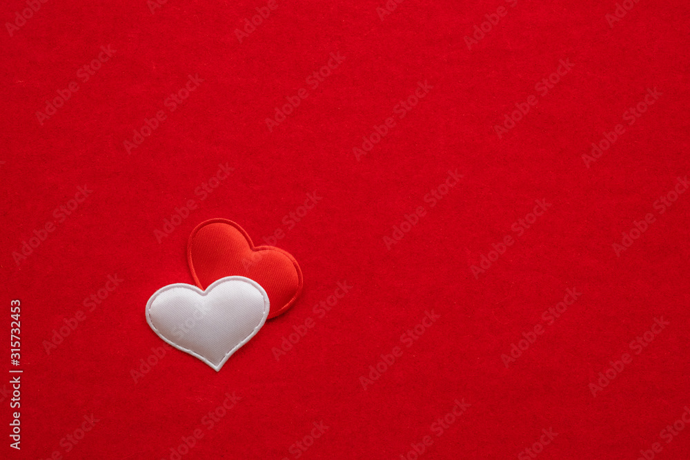 2 small textile hearts, white and red, are nearby on a background of red velvet paper. 2 small textile hearts, white and red, are nearby on a background of red velvet paper.