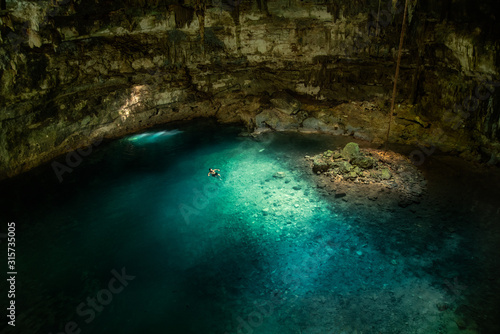 Man swims in the cool blue underground cave waters of Mexican cenote 