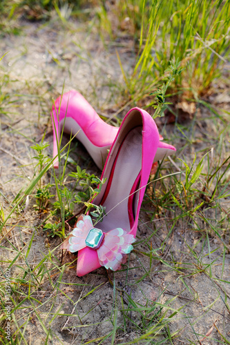 Fancy pink high heels lying in the grass. Fashion still life in nature. Trendy pink heels with fashion ribbon. Wedding shoes detail. 