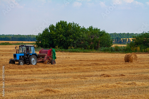 A tractor with a trailed bale making machine collects straw rolls in the field and makes round large bales