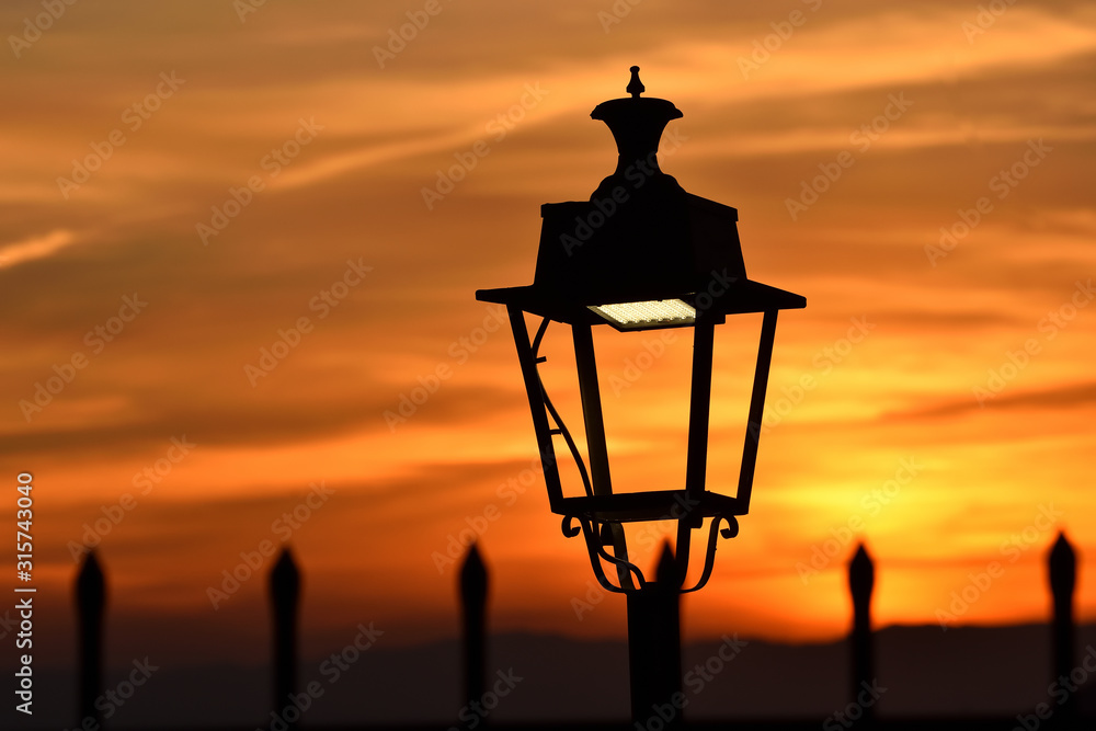 Natural sunset light next to that produced by led bulbs in a lamppost Natural sunset light next to that produced by led bulbs in a lamppost