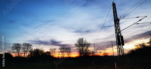 A fantastic sunset with red yellow orange and purple tones with dramatic cloud formation over green meadows with bare trees in January on the island of Rügen