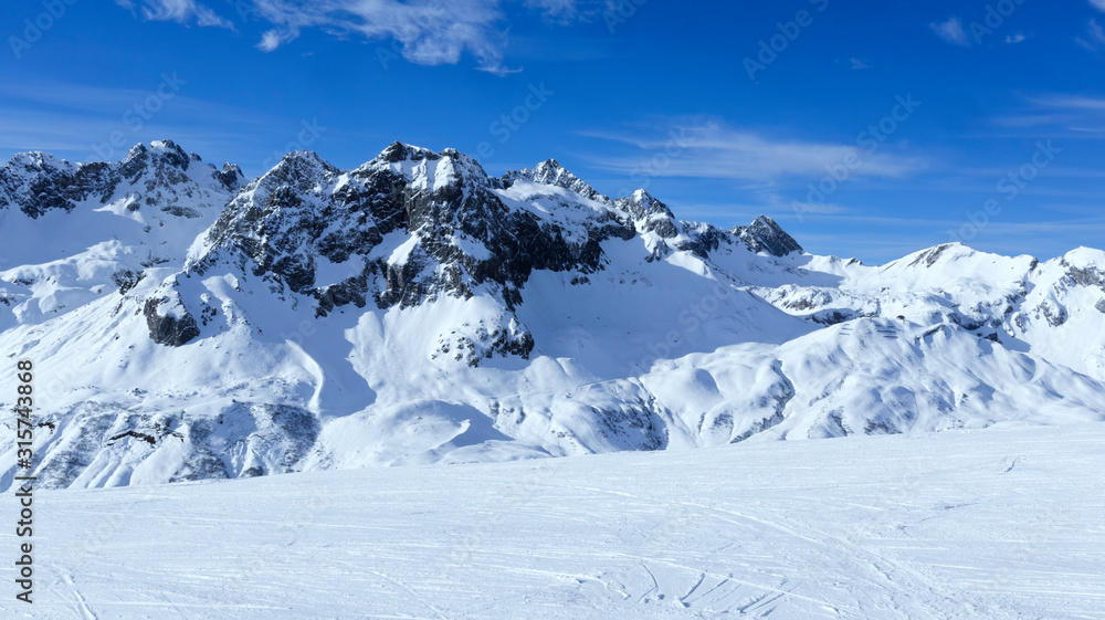 Alpine snowy peaks panorama with slopes, off piste on fresh powder in Zurs winter sport resort, Alps, Arlberg, Austria, on a sunny cold day .