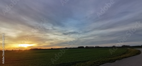 A fantastic sunset with red yellow orange and purple tones with dramatic cloud formation over green meadows with bare trees in January on the island of Rügen
