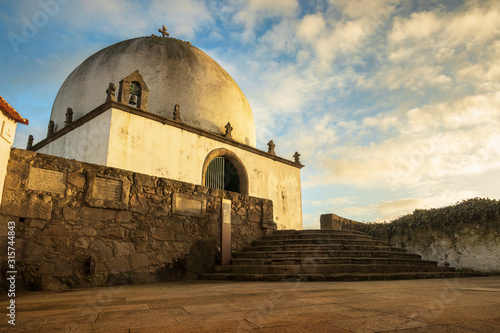 Socorro Chapel in Vila do Conde, Portugal, lit by the sunset and a sky with clouds in the background.