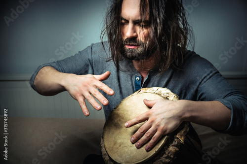 Leinwand Poster Long-haired man playing an ethnic percussion musical instrument jembe
