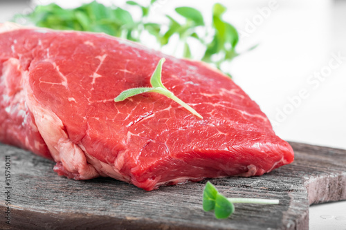 Fresh juicy piece of fresh beef with greens on a wooden Board on a white wooden background.