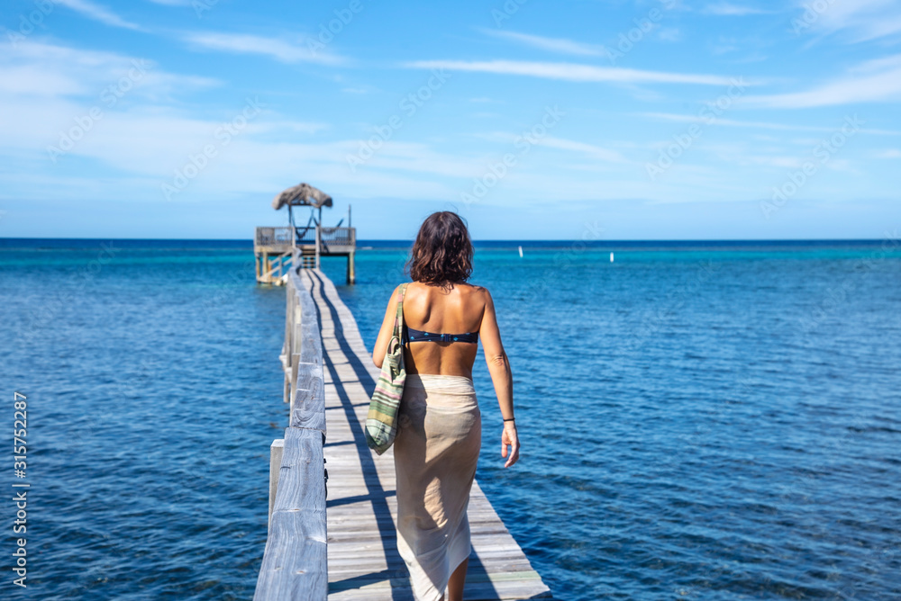 A young woman walking along a wooden walkway along the beach of Sandy Bay on Roatan Island. Honduras