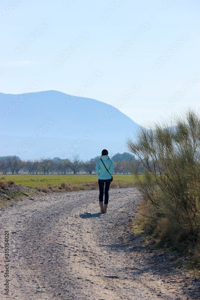 young woman walking on the road in the field with mountains on the background