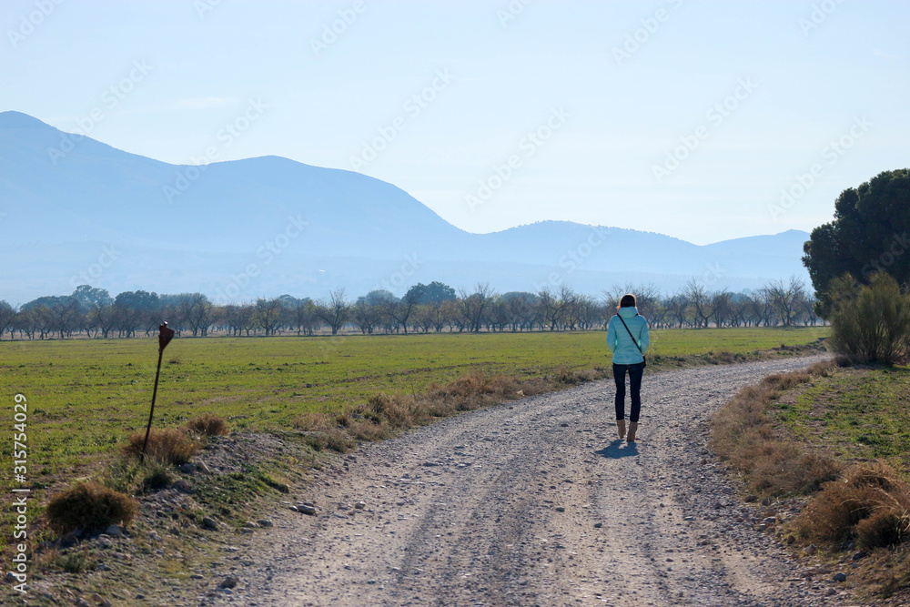 young woman walking on the road in the field with mountains on the background