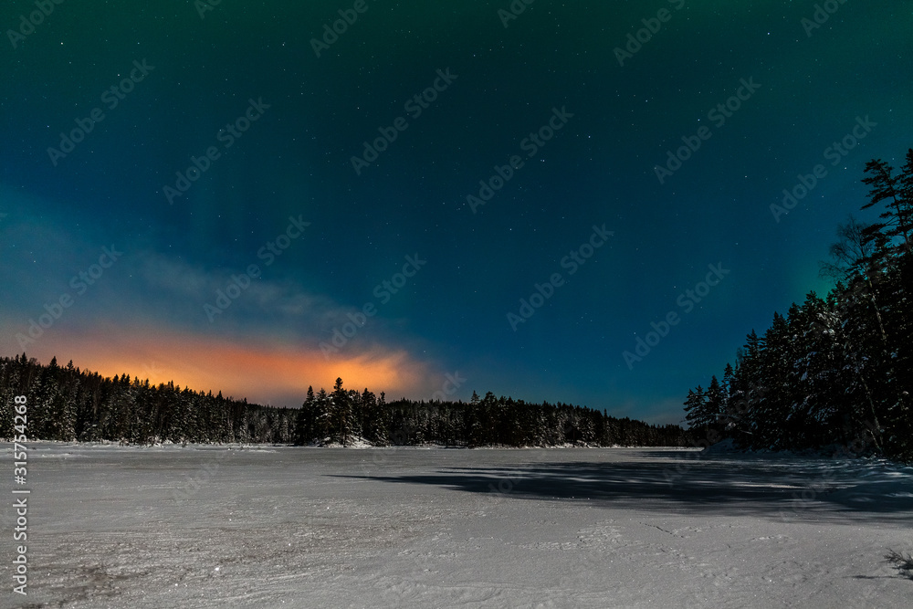 Dramatic polar lights, Aurora borealis with many clouds and stars by moonlight on the sky over a frozen lake and snowy forest in Sweden. long shutter speed.