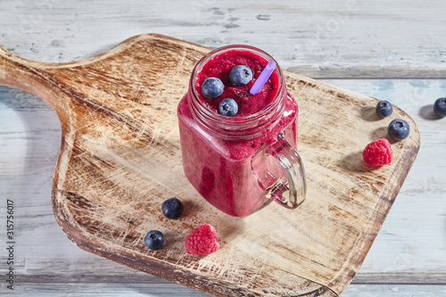 Fruit pink smoothie with berries in a glass jar on a wooden white table. Refreshing and healthy summer drink. Copy space