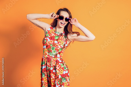 Girl in floral dress emotionally poses on the orange background.
