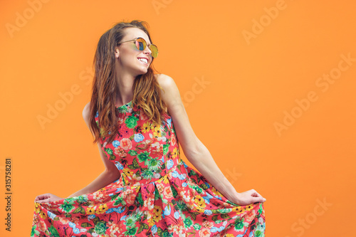 Girl in floral dress emotionally poses on the orange background.