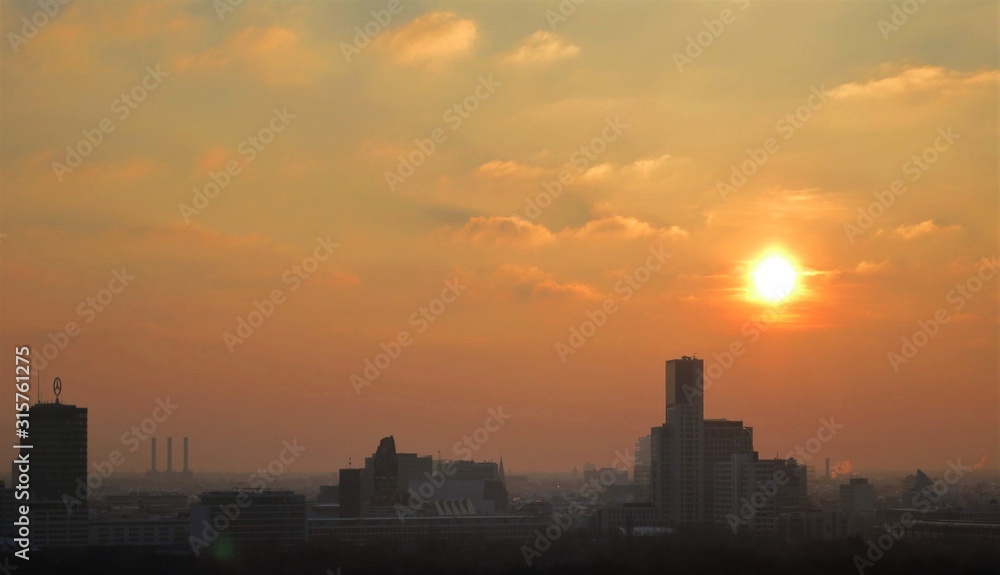 Panoramaansicht mit urbanem Horizont über Berlin am Abend mit untergehender Sonne im Winter, die den Himmel über der Stadt in orange, gelbes stimmungsvolles Licht taucht