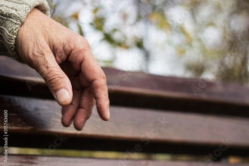 The lonely older hand of a man. An older man sitting on a bench, bokeh background, outdoors