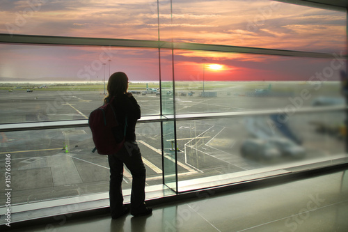 female passenger, waiting for his flight, stands at the window and looks at the airport runway, a travel concert